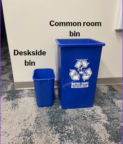 A short blue deskside bin sits to the right of a tall, blue common room bin for recycling.