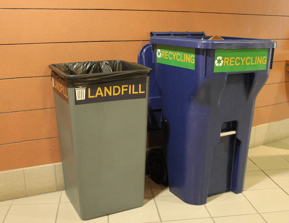 A gray bin labeled landfill positioned next to a blue toter labeled recycling.
