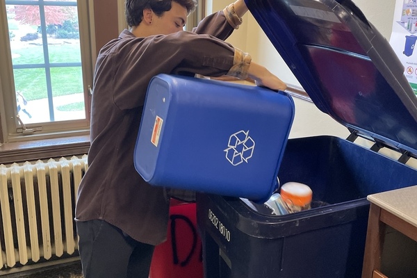 Male student emptying personal recycling bin into recycling toter.