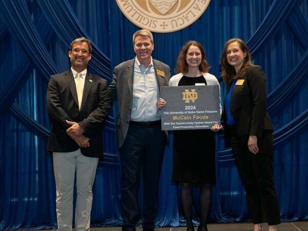 Four people stand on a stage holding an award in front of the Notre Dame Crest