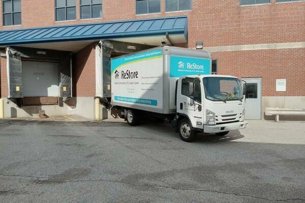A Habitat for Humanity ReStore box truck is parked near a receiving garage door.