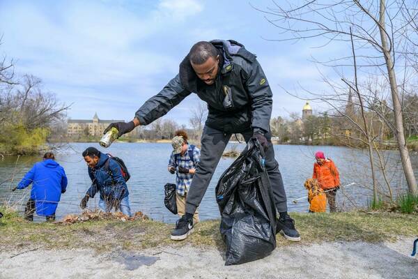 Person bending over to pick up aluminum can and throw it away during a litter pick-up near St. Mary's Lake